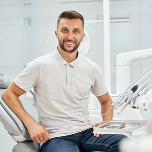 Man in grey polo smiling sitting up in dental chair