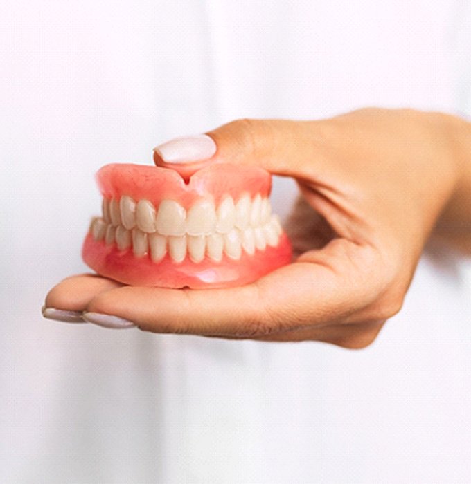 Closeup of dentist holding dentures in Lansing