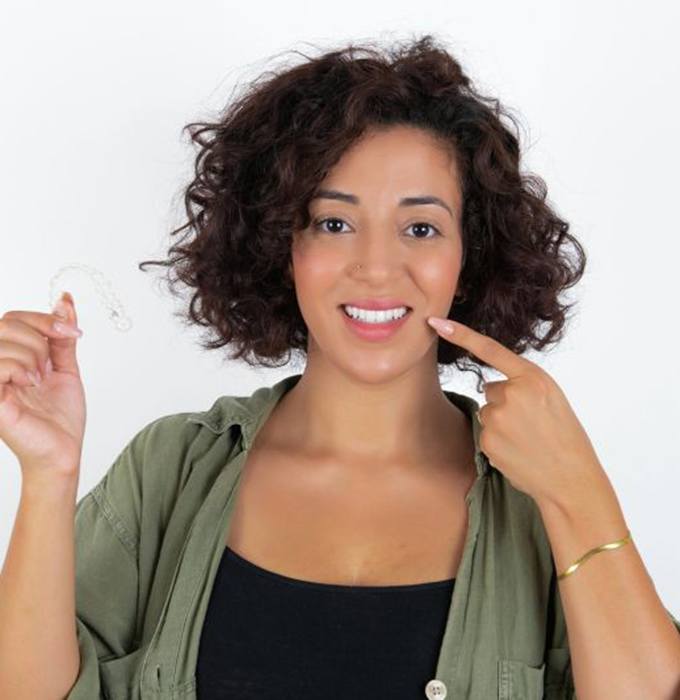 Woman holding her clear aligner and pointing at her teeth