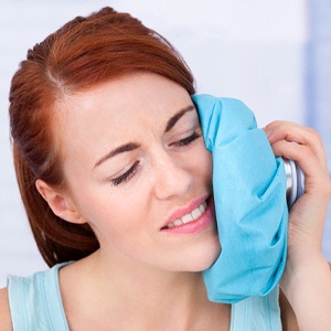 Woman using cold compress after getting dental implants in Lansing