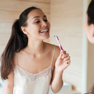 Woman brushing teeth with dental implants in Lansing