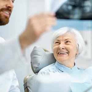 Older woman smiling in dental chair looking at x-ray