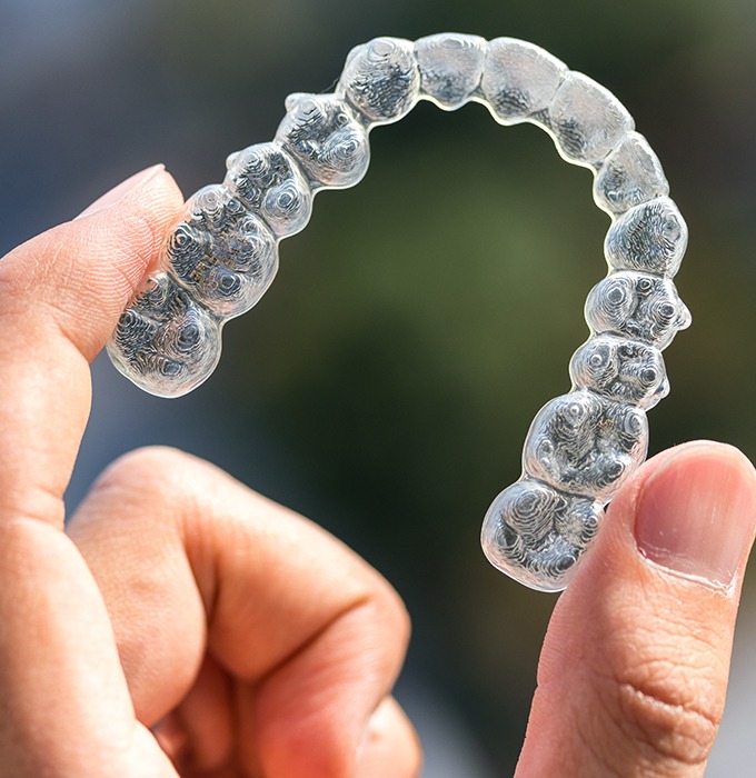 Hand holding up an Invisalign clear braces tray