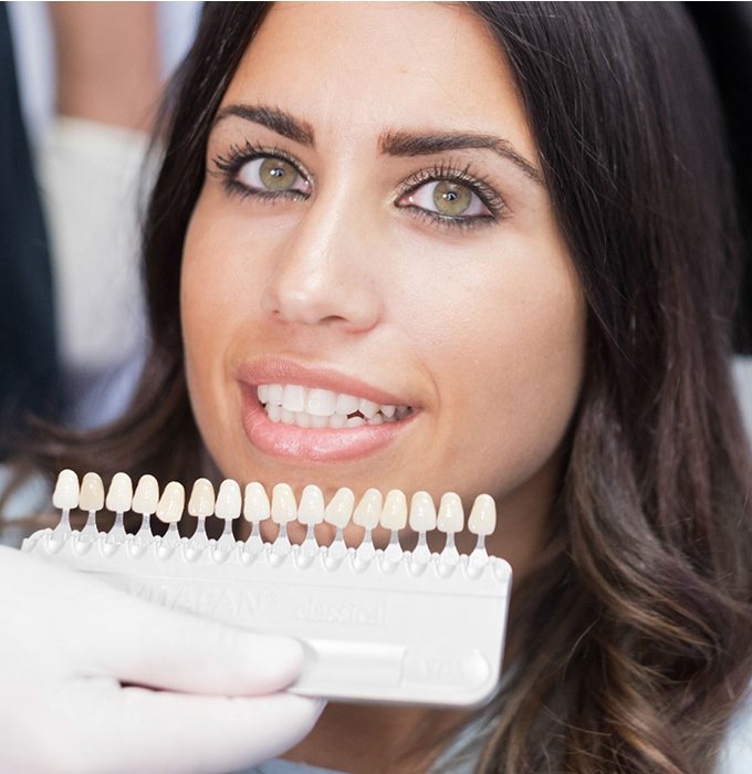 dentist holding a row of veneers up to a patient’s smile 