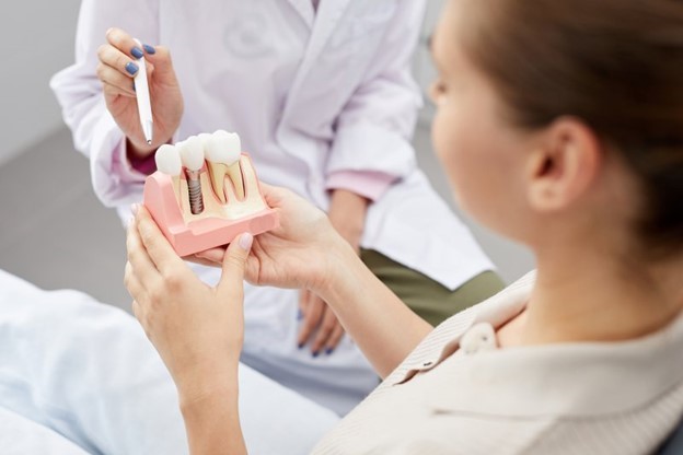 patient at dentist holding dental implant model